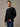 A man wearing a black long-sleeve flannel and blue jeans, standing against a textured gray studio background. Upgraded fabric: softer, thicker waffle, better shape retention.