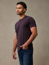 man wearing a deep mulberry colored short-sleeve crewneck t-shirt and blue jeans, standing 