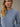 A close-up shot of a woman wearing a skyline blue waffle-knit thermal top against a neutral beige background. Relaxed drop-shoulder fit, never tight or restrictive.