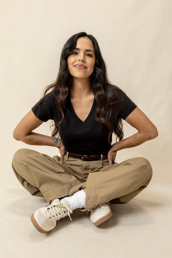Woman sitting on the floor wearing a black v-neck top and beige pants - softness you can feel