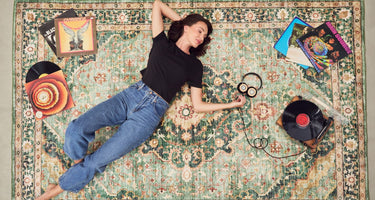 woman wearing black boxy tee with denim jeans, listening to records on a rug