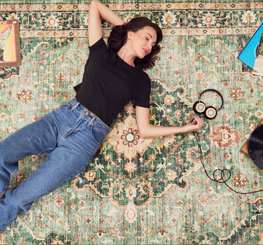 woman wearing black boxy tee with denim jeans, listening to records on a rug